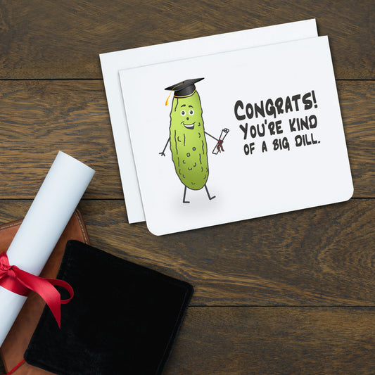 A photo of a graduation card. It has a pickle on it. It's wearing a graduation cap and holding a scroll. Text on card reads, 'Congrats! You're kind of a big dill.'