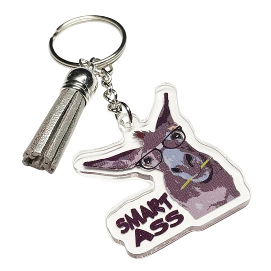 A photo of a vinyl keychain. It has a donkey on it with a pencil in its mouth; it's wearing glasses. Text reads, 'Smart Ass.'