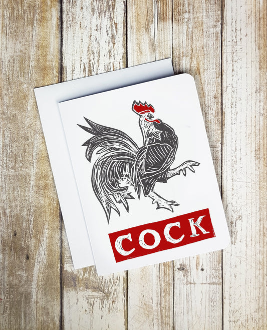 A photo of a white card. It has a strutting cockerel on it. Text on card reads 'COCK.'