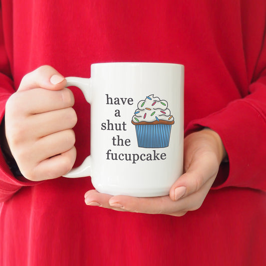 A photo of a funny mug. It has a cartoon cupcake on it. Text next to cupcake reads 'Have a shut the fucupcake.'