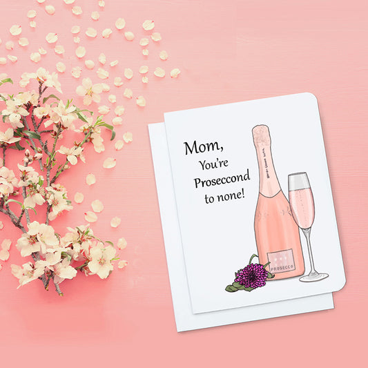 A photo of a mothers day card. It has an illustration of a bottle of pink Prosecco on it. Text reads, Mom, You're Proseccond to None!