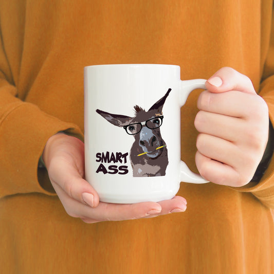 A photo of a funny mug. It has a cartoon donkey on it. The donkey is wearing glasses and has a pencil in its mouth. Text on mug reads 'Smart Ass.'