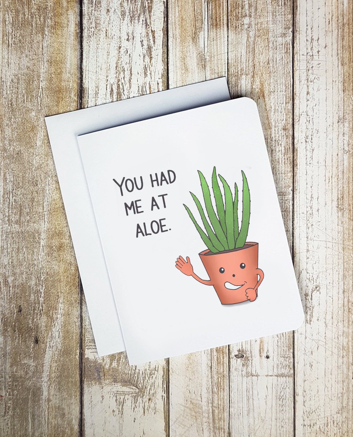 A photo of a white card. It has a cartoon aloe plant on it waving. The plant is saying 'You had me at Aloe.'