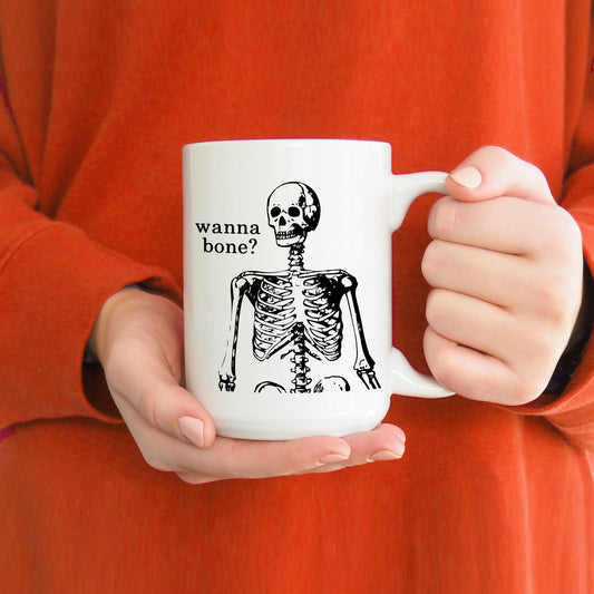 A photo of a funny mug. It has a cartoon skeleton on it. Text on mug reads, 'Wanna Bone?'
