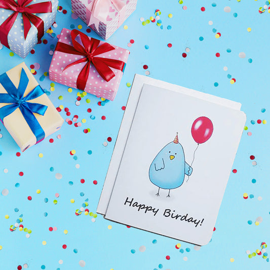 A photo of a white birthday card. It has a blue cartoon bird on it. It's holding a red balloon and wearing a party hat. Text on card reads, 'Happy Birday!'
