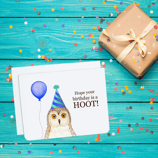 A photo of a white birthday card. It has an illustrated owl on it. It's wearing a party hat and holding a balloon. Text on card reads, Hope your birthday is a hoot!