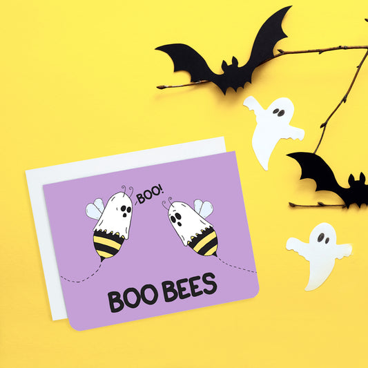 A photo of a lilac greeting card. It has cartoon bees with sheets on their heads. One is saying 'Boo' to the other. Text at the foot of the card reads, 'Boo Bees.'