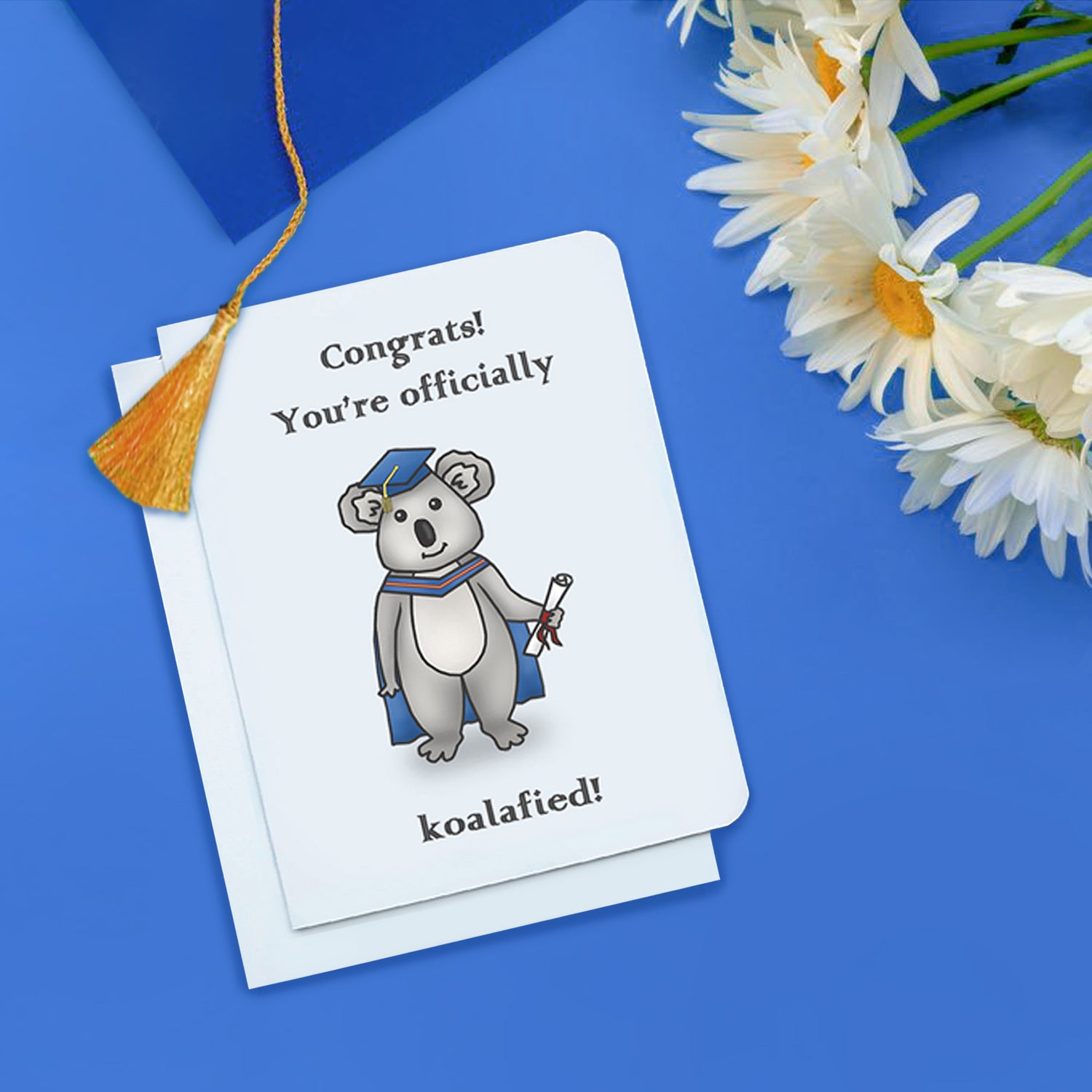 A photo of a white graduation card. It has a cartoon koala bear on it. It is wearing a graduation cap and holding a scroll. Text on card reads, Congrats! You're officially koalafied!'