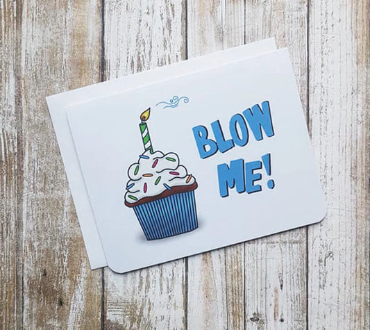 A white birthday card. It has a blue cupcake with a candle in it. Big blue text reads 'Blow Me!'