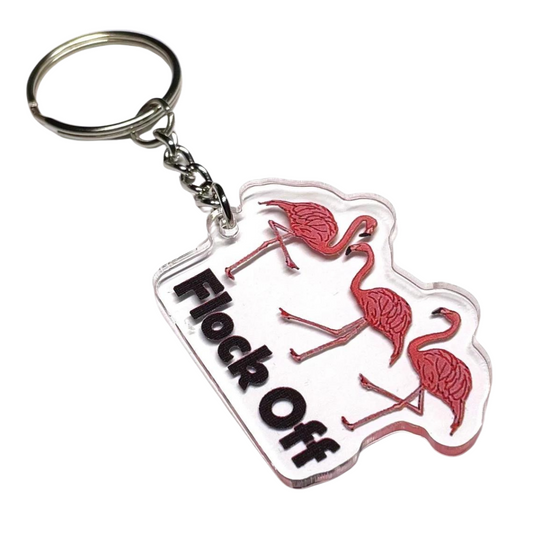 A photo of a vinyl keychain. It has three flamingoes on them. Text below flamingos reads "Flock Off.'