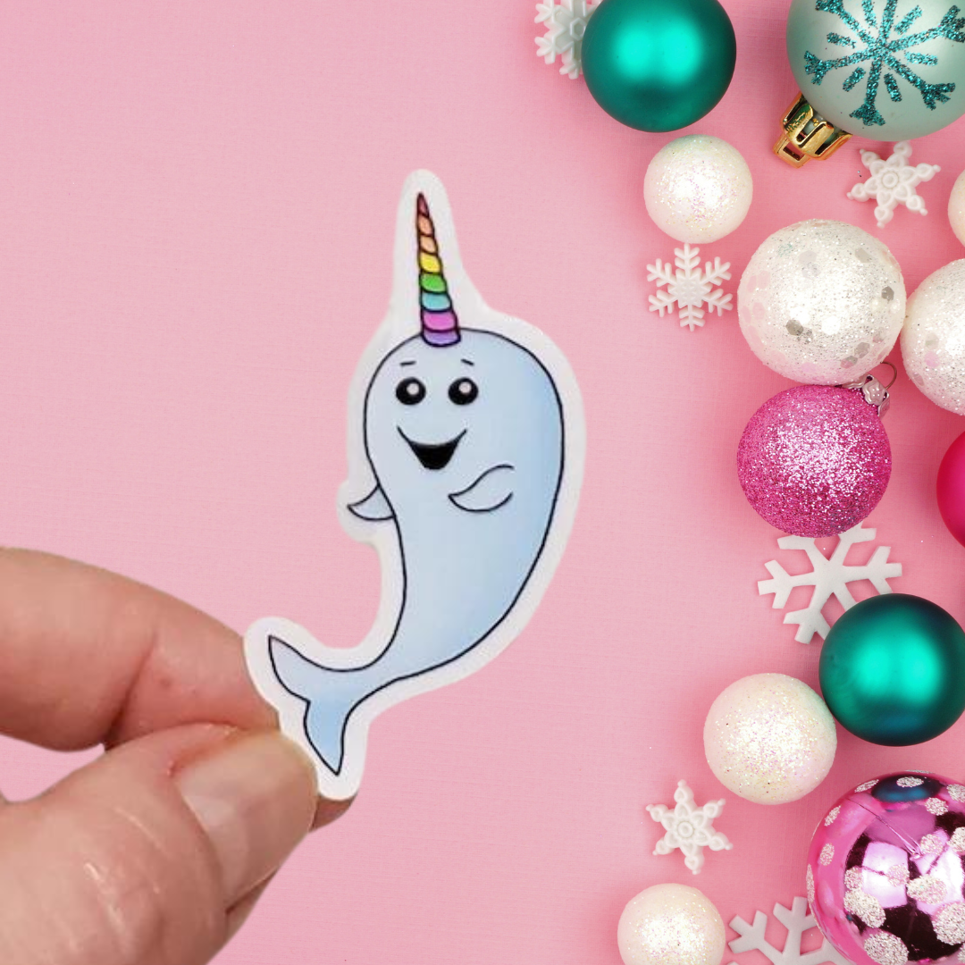 A photo of a cute sticker. It has a smiling cartoon narwhal with a striped unicorn horn.