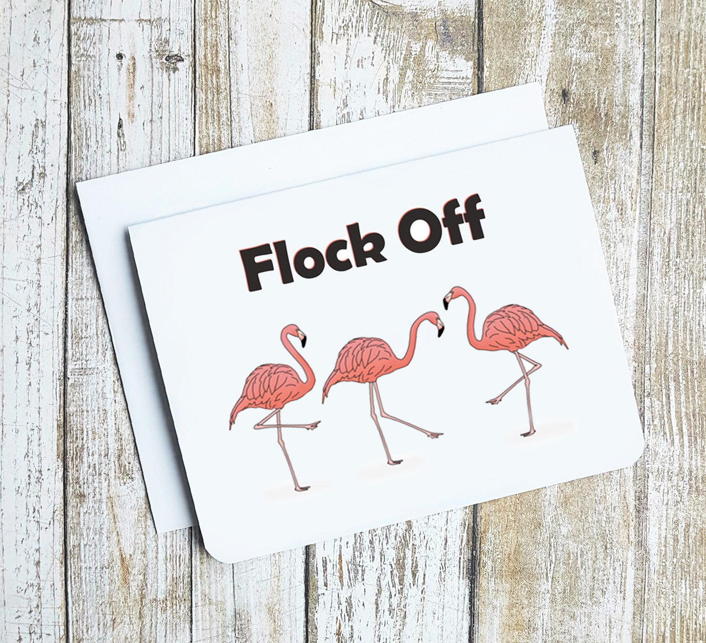 A photo of a greeting card. It has three flamingos on it. Text above reads, Flock Off.