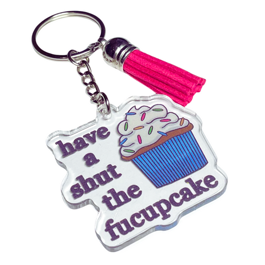A photo of a vinyl keychain. It has a cupcake with sprinkles on it. Text reads, Have a shut the fucupcake.