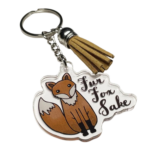 A photo of a vinyl keychain. It has a cartoon fox on it. Text on keychain reads, 'Fur Fox Sake.'