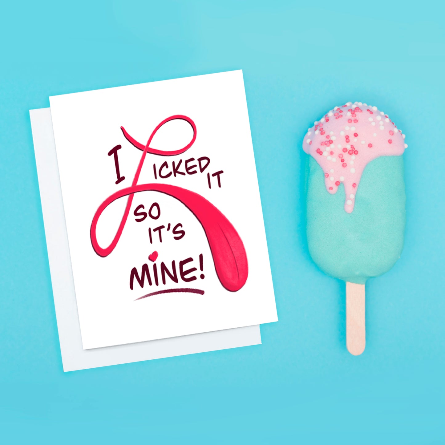 A photo of a white Valentine's card. It says in big colourful red and pink text, 'I Licked It So It's Mine.' the L of the word, 'licked' is a tongue.