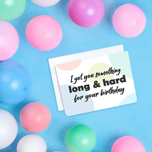 A photo of a birthday card. It has circles of pastel colours in the background. Text on card says, I got you something long & hard for your birthday.'