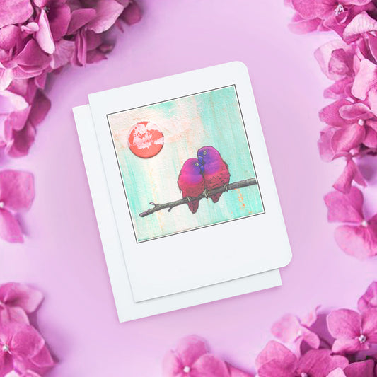A photo of an illustrated valentine's card. It has two little purple and pink lovebirds sitting on a branch in the foreground, with a pale blue background and a red sun.