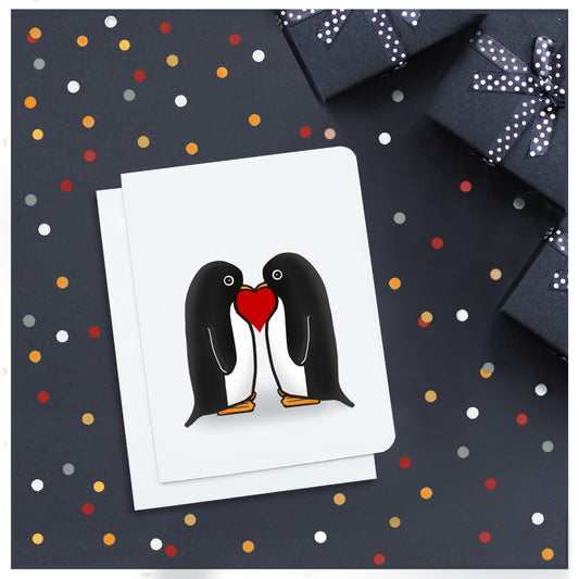 A photo of a cute card. It has two cartoon penguins on it facing each other. There's a red love heart between them.