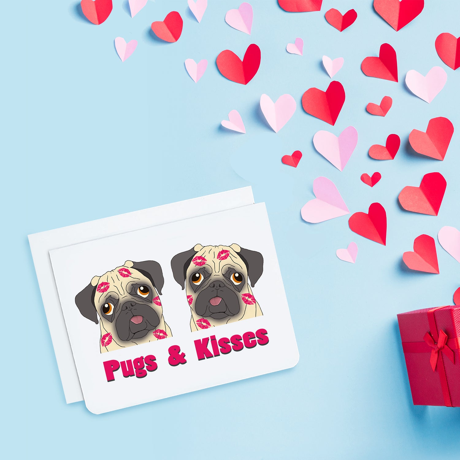 A photo of a white greeting card. It has two cartoon pugs on it. They're covered in lipstick kisses. Text below on card reads, 'Pugs & Kisses.'