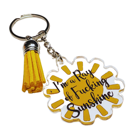 A photo of a vinyl keychain. It has a yellow sunshine on it. Text reads 'I'm a ray of fucking sunshine'