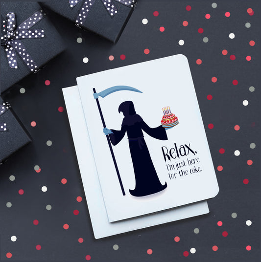 A photo of a white birthday card. It has a grim reaper on it holding a birthday cake. Text on card reads, 'Relax, I'm just here for the cake.'