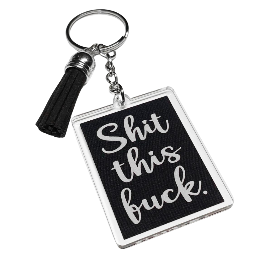 A photo of a fun keychain. It's a black rectangle, Text on it reads 'Shit this fuck.'