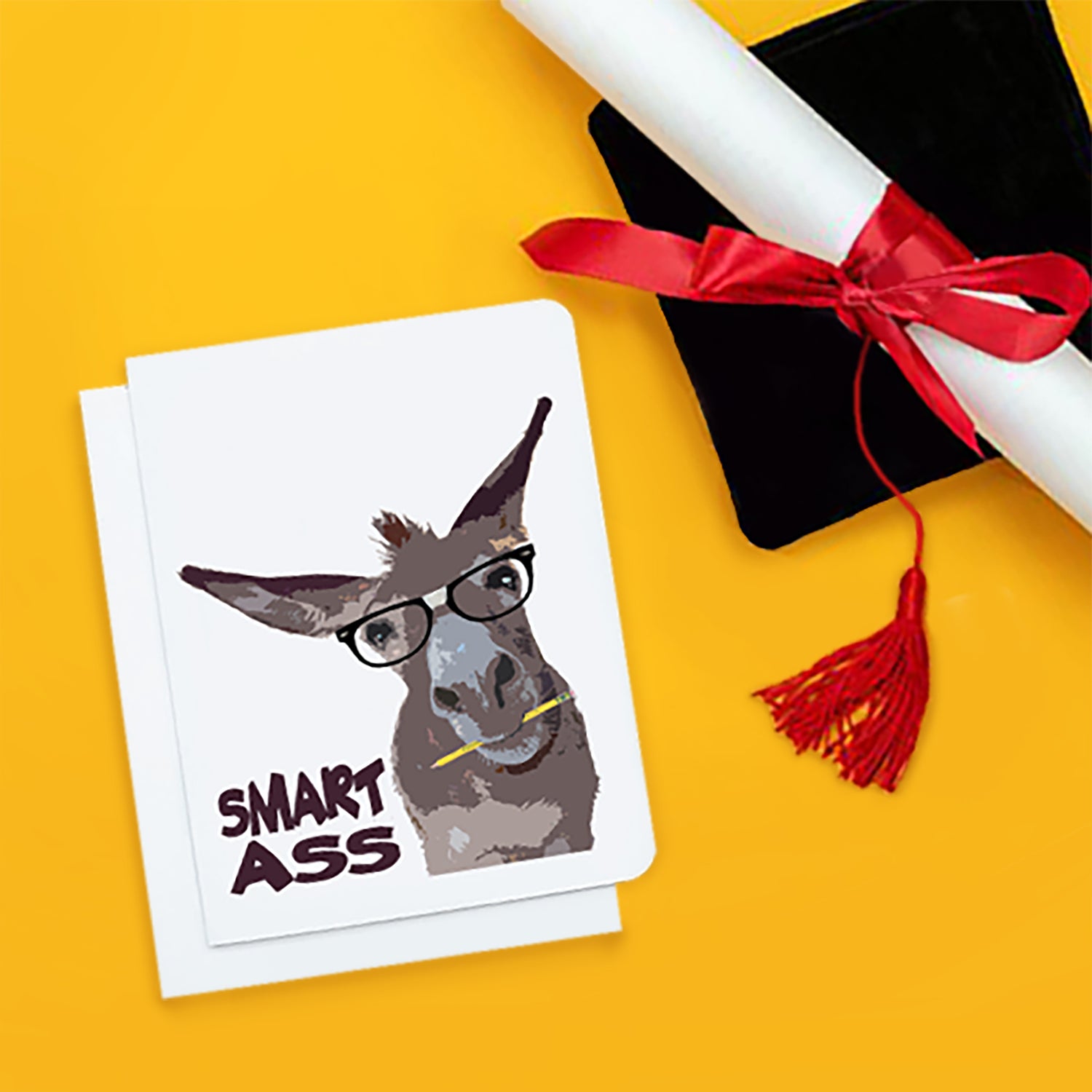 A photo of a white graduation card. It has a donkey on it. It has glasses on and a pencil in its mouth. Text on card reads, 'Smart Ass.'