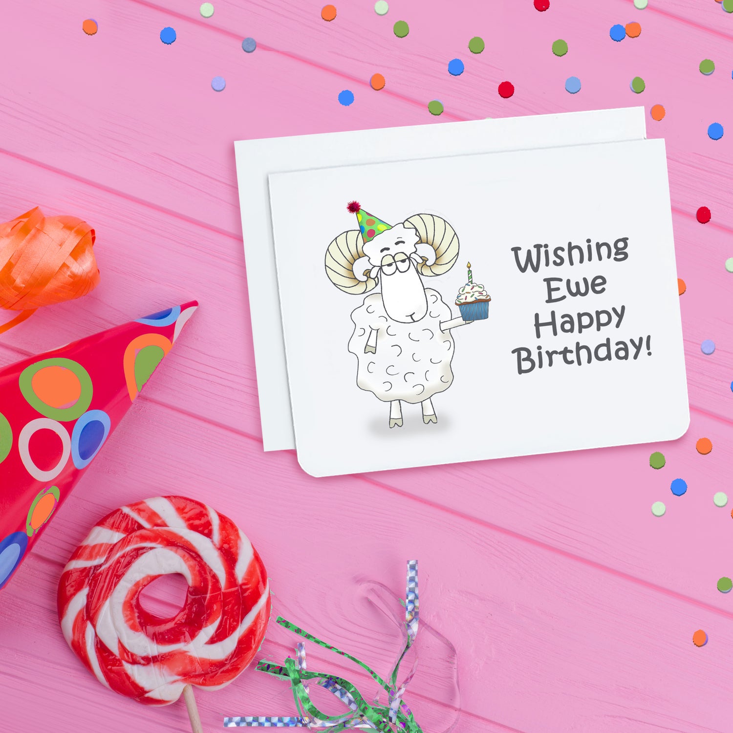 A photo of a white birthday card. It has a cartoon sheep on it. It's holding a cupcake. Text on card reads, 'Wishing Ewe Happy Birthday.