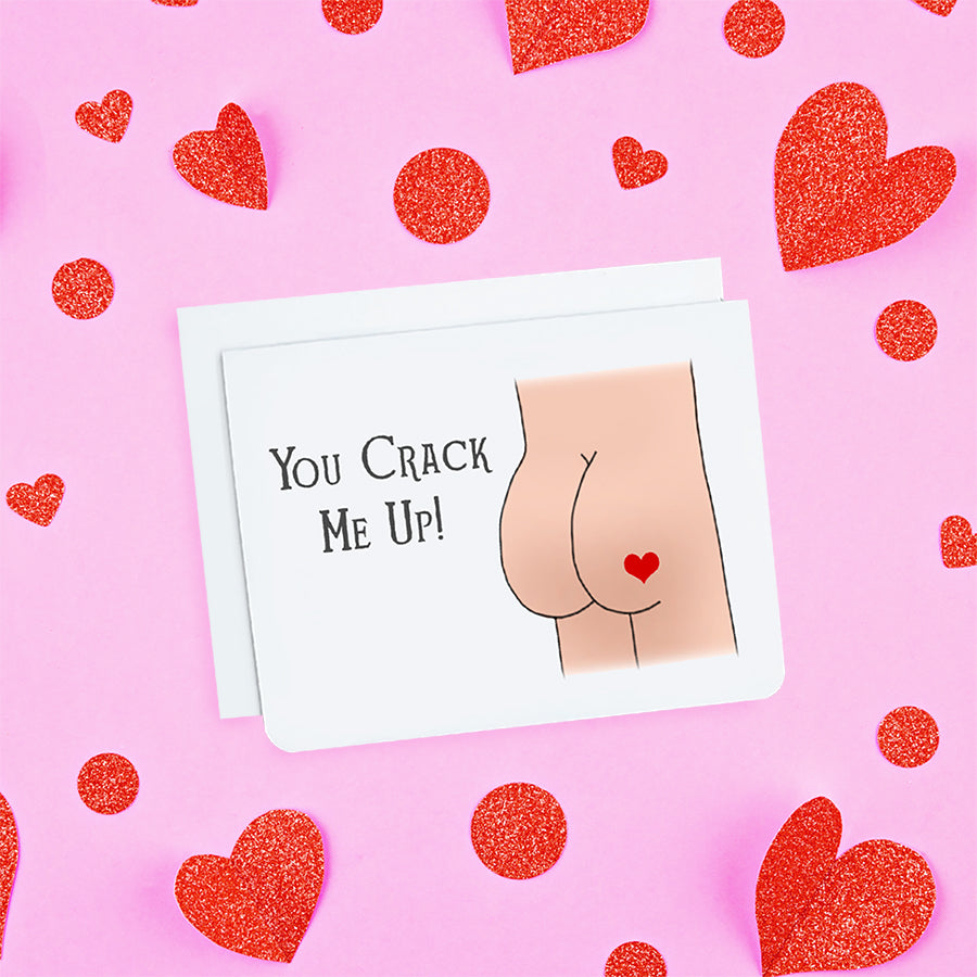 A photo of a white greeting card. It has a cartoon butt on it. The one butt cheek has a red love heart on it. Text on card reads 'You Crack Me Up.'