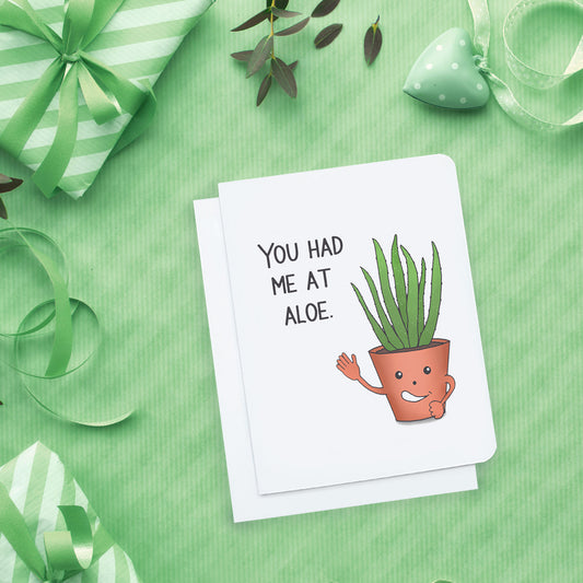 A photo of a white card. It has a cartoon aloe plant on it waving. The plant is saying 'You had me at Aloe.'