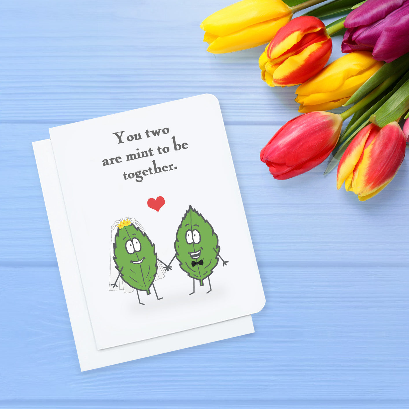 A photo of a greeting card. It has two cartoon mint leaves on it. One has a veil on, the other, a bowtie. Text reads, 'You two are mint to be together.'