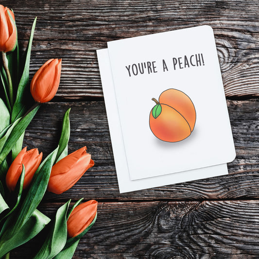 A cute card. It has a cartoon peach on it. Text above on card reads 'You're a peach.'