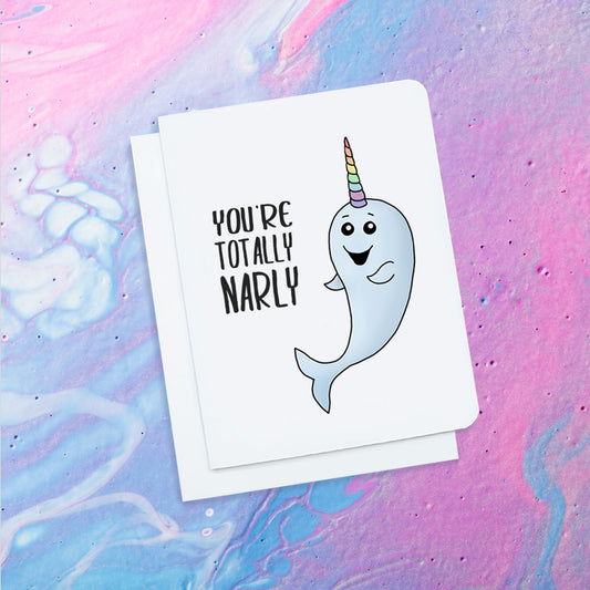 A cute white greeting card. It has a smiling cartoon narwhal on it with a striped colourful horn. Text on card reads 'You're Totally Narly.'