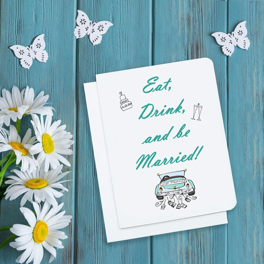 A photo of a white wedding card. It says, 'Eat, Drink and be Married,' in teal script font. There's an illustrated car at the bottom dragging cans.