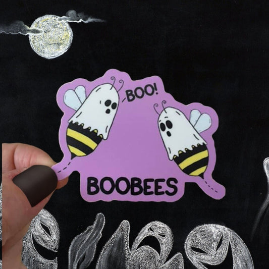 A photo of a cute sticker. It has two cartoon bees on it with sheets over their heads. One is saying 'Boo!' to the other. Text on sticker reads 'BooBees.'