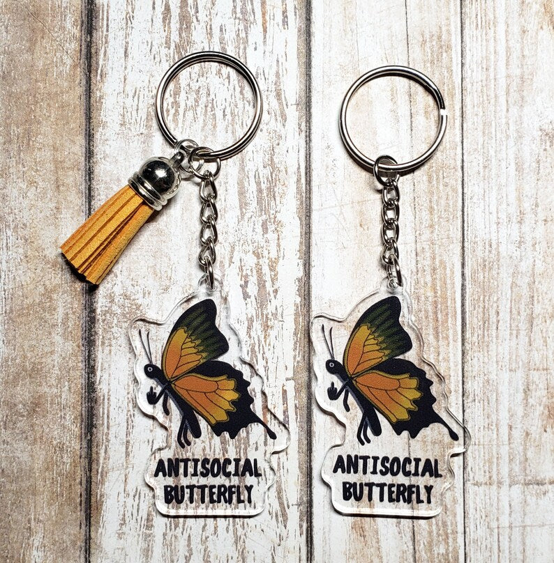 A photo of two acrylic keychains. On the keychain are monarch butterflies giving the middle finger. Text below on keychain reads 'Antisocial Butterfly.'
