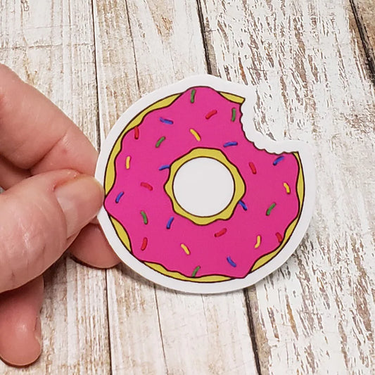 A photo of a cute sticker. It's a pink sprinkle donut with a bite out of it.