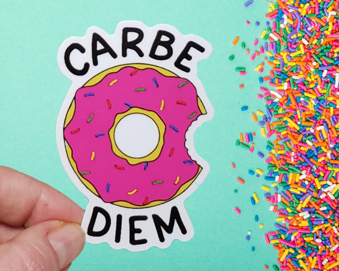 A photo of a sticker. The sticker is of a pink cartoon donut. Text on sticker reads 'Carbe Diem.'