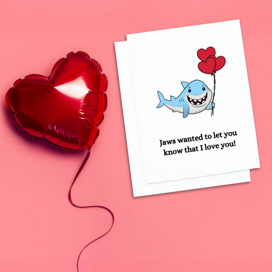 Valentines card. A smiling shark holding red balloons. text reads, Jaws wanted to let you know that I love you.