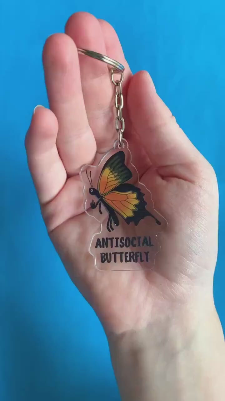 A video of a hand showing off a monarch butterfly giving the middle finger. Text below on keychain reads 'Antisocial Butterfly.'