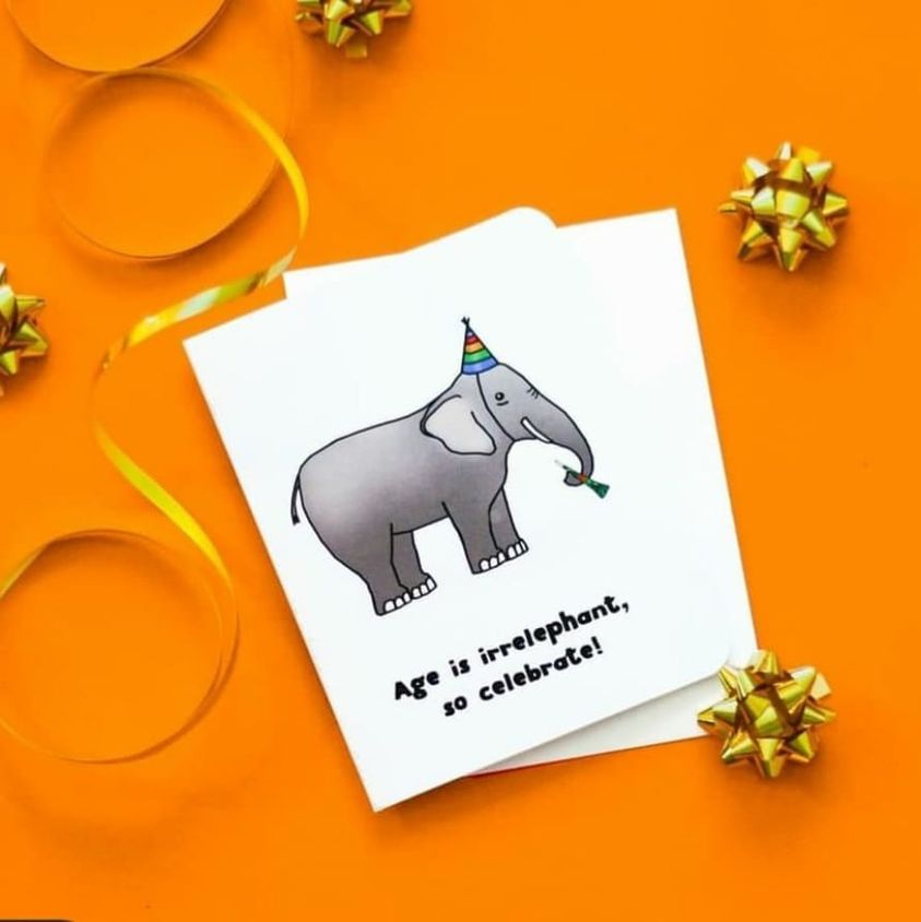 A photo of a white birthday card. It has a cartoon elephant on it wearing a party hat. It has a party horn in its trunk. Text on card reads, 'Age is irrelephant, so celebrate!'