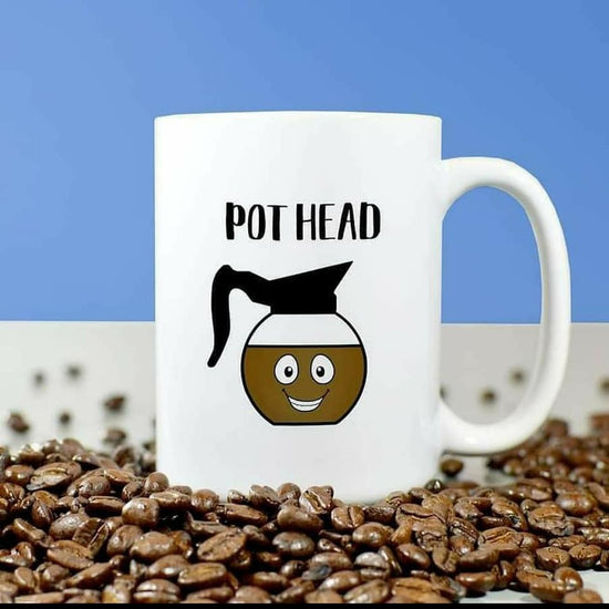 A photo of a funny mug. It has a cartoon graphic of a smiling coffee pot on it. Text on mug reads 'Pot Head.'