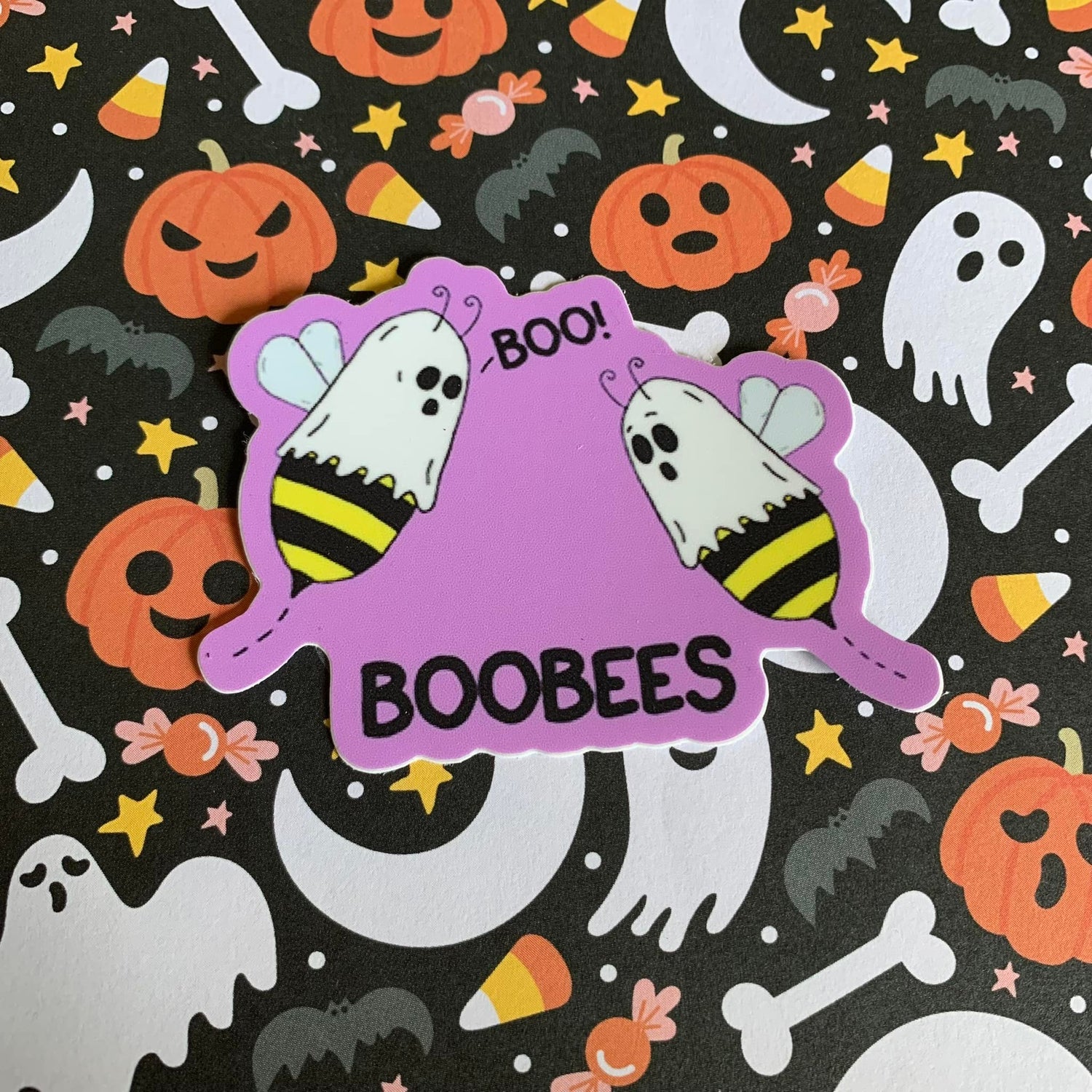 A photo of a sticker of two cartoon bees with sheets on their heads. Text on sticker reads 'BooBees.'