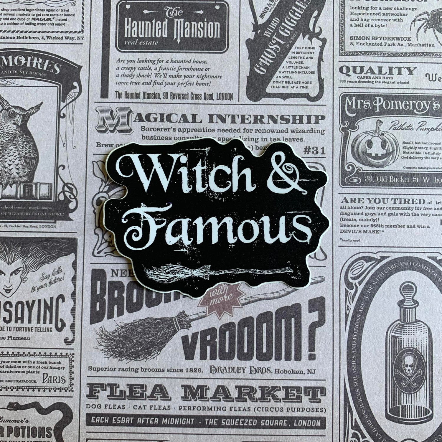 A photo of a vinyl sticker. It's black. White gothic font reads 'Witch & Famous.'