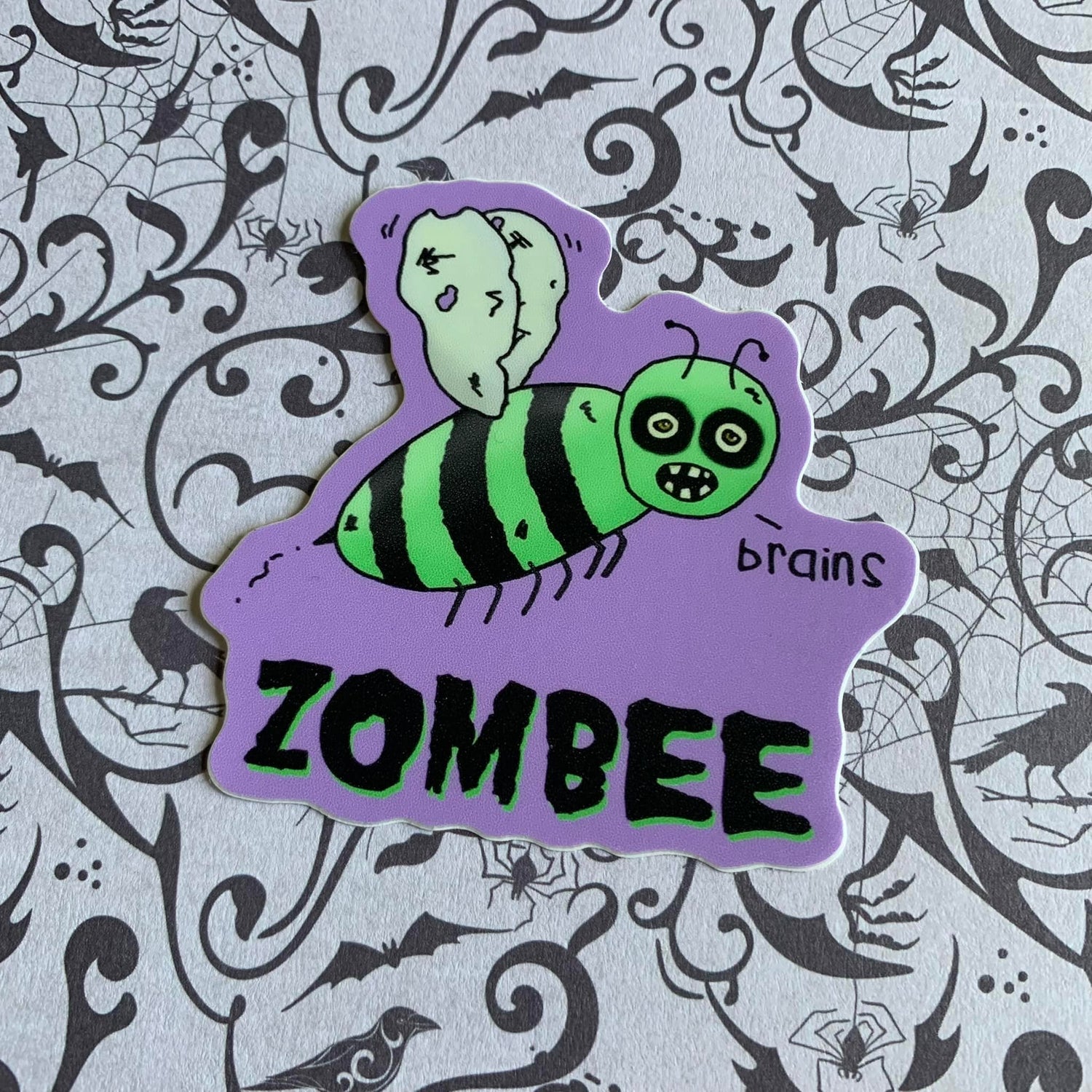 A photo of a fun sticker. There's a green dishevelled cartoon bee on it. Text below reads 'Zombee.'