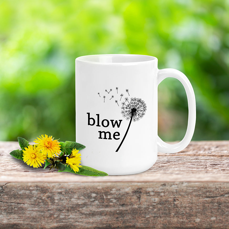 A photo of a white mug with a blown dandelion on it. Text below reads 'Blow Me.'