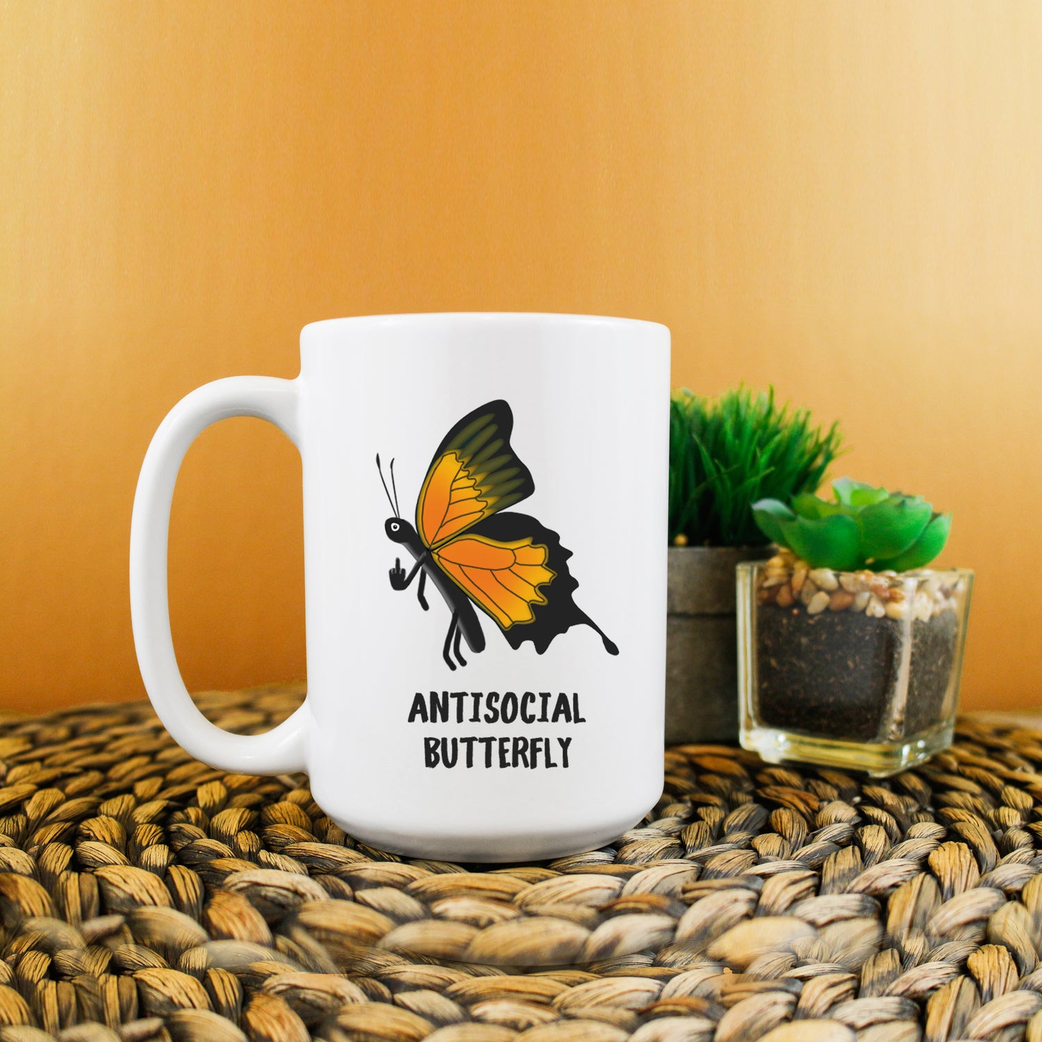 A photo of a white mug. On the mug is a cartoon butterfly with its finger up. Text on mug below image reads 'Antisocial Butterfly.'