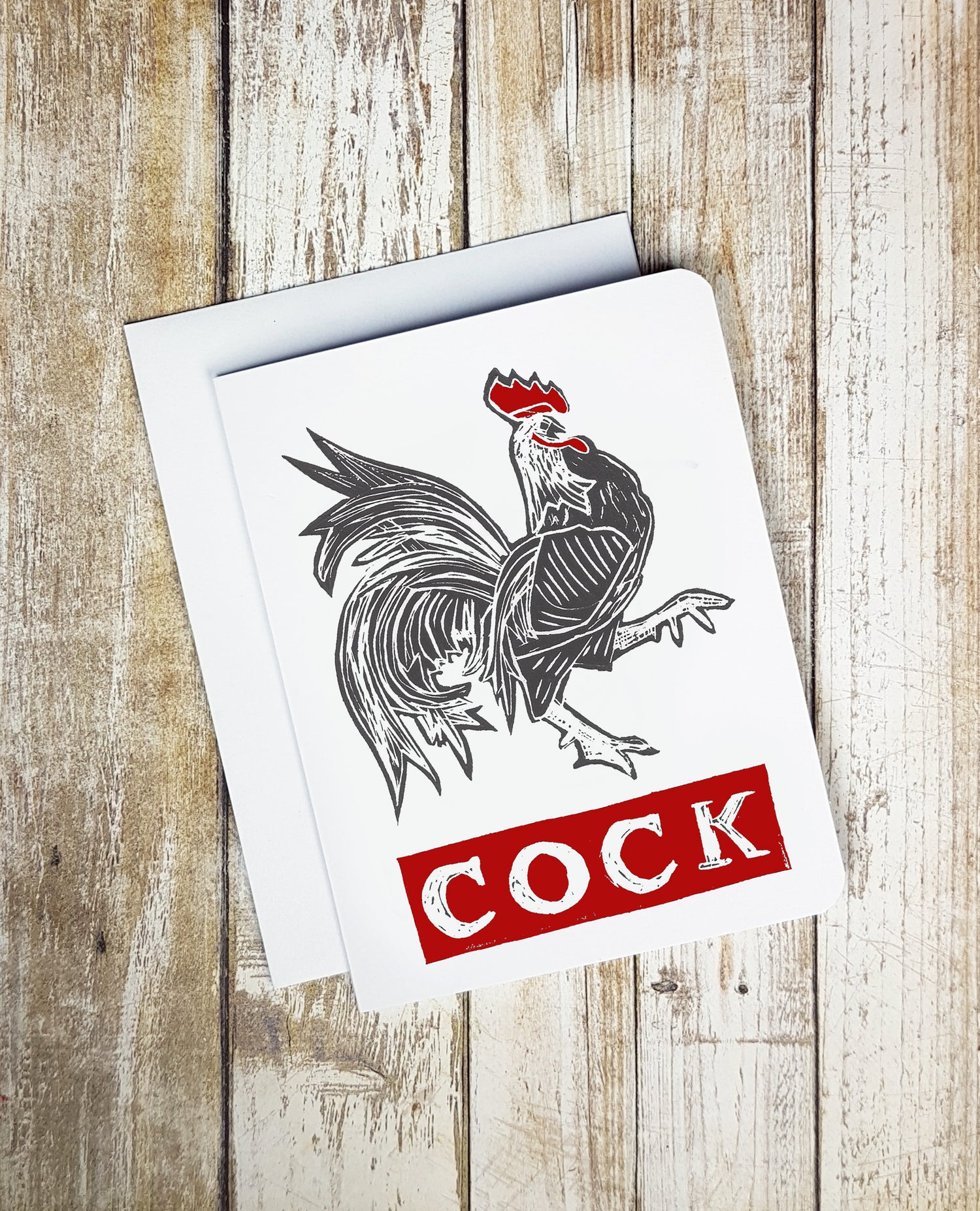 A photo of a white card. It has a strutting cockerel on it. Text on card reads 'COCK.'