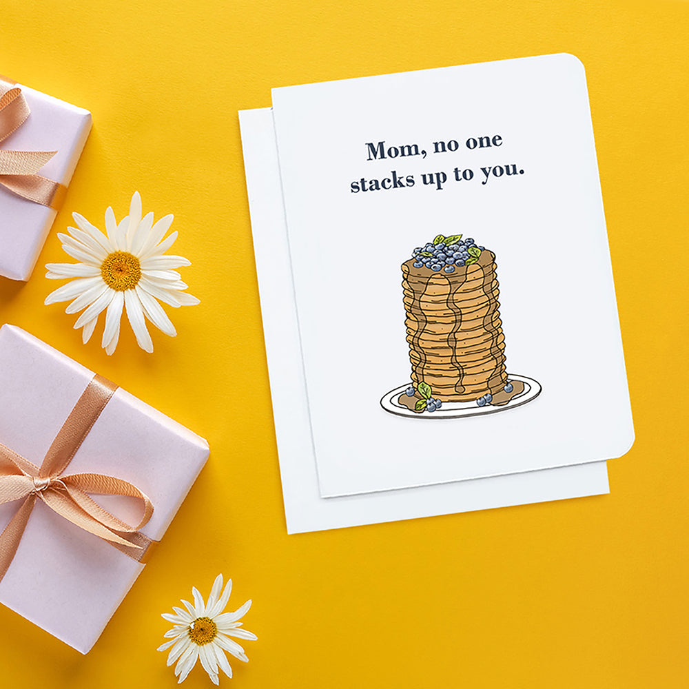 A photo of a mothers day card. It has a stack of pancakes on it. Text reads, Mom, no one stacks up to you.