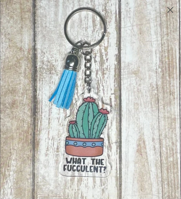 A photo of a key chain. It has a succulent on it. Text below on keychain reads 'What the Fucculent?'